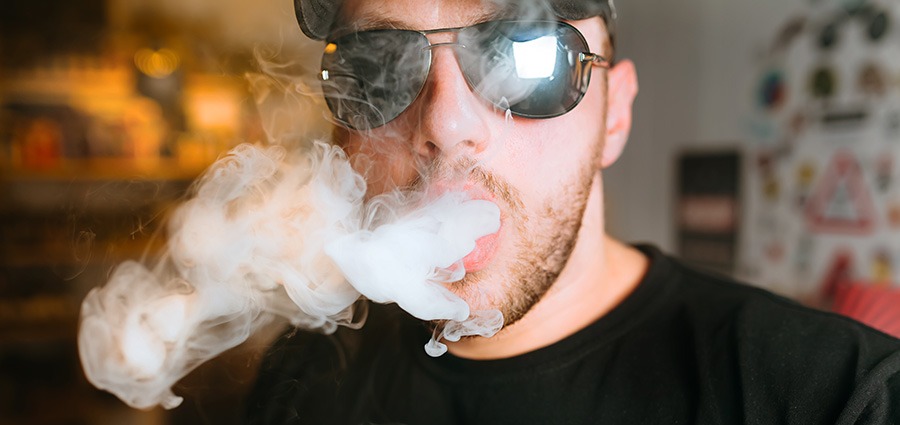Man with sunglasses blowing vape clouds after smoking shatter weed. online dispensary mail order marijuana weed online.