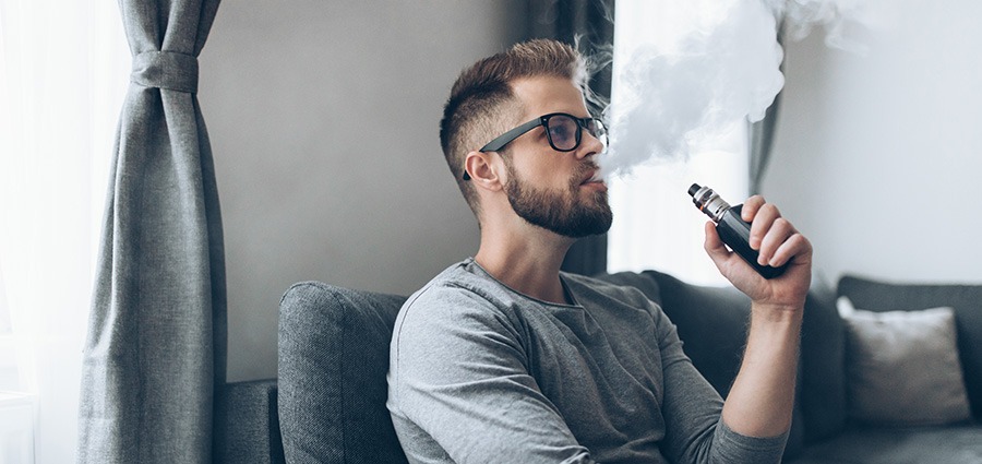 Man on sofa at home using a weed pen disposable vape from an online dispensary for BC cannabis and BC bud online.
